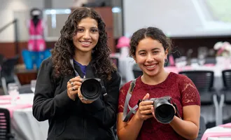 two female youth holding camers and smiling 
